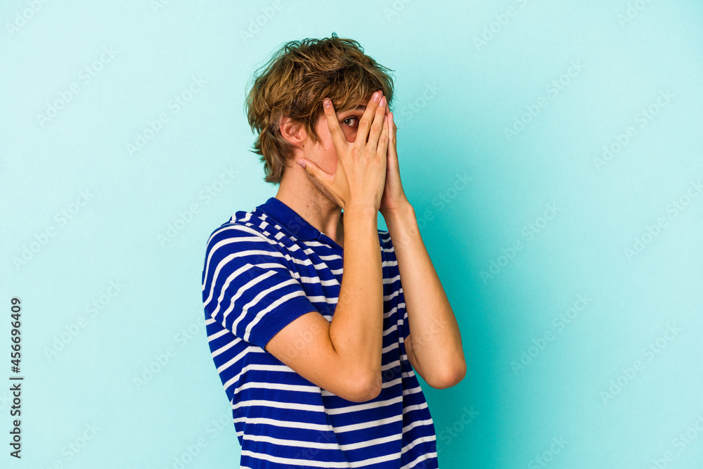 Young caucasian man with make up isolated on blue background blink through fingers frightened and nervous. Young caucasian man with make up isolated on blue background blink through fingers frightened and nervous.