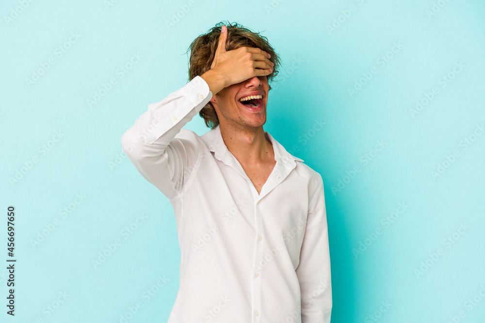 Young caucasian man with make up isolated on blue background covers eyes with hands, smiles broadly waiting for a surprise. Young caucasian man with make up isolated on blue background covers eyes with hands, smiles broadly waiting for a surprise.