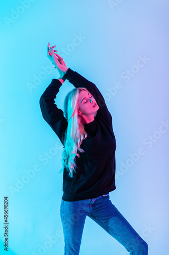 Fototapeta Naklejka Na Ścianę i Meble -  Fashionable beautiful sensual blonde woman in black hoodie with stylish blue jeans on multicolored neon pink light in studio