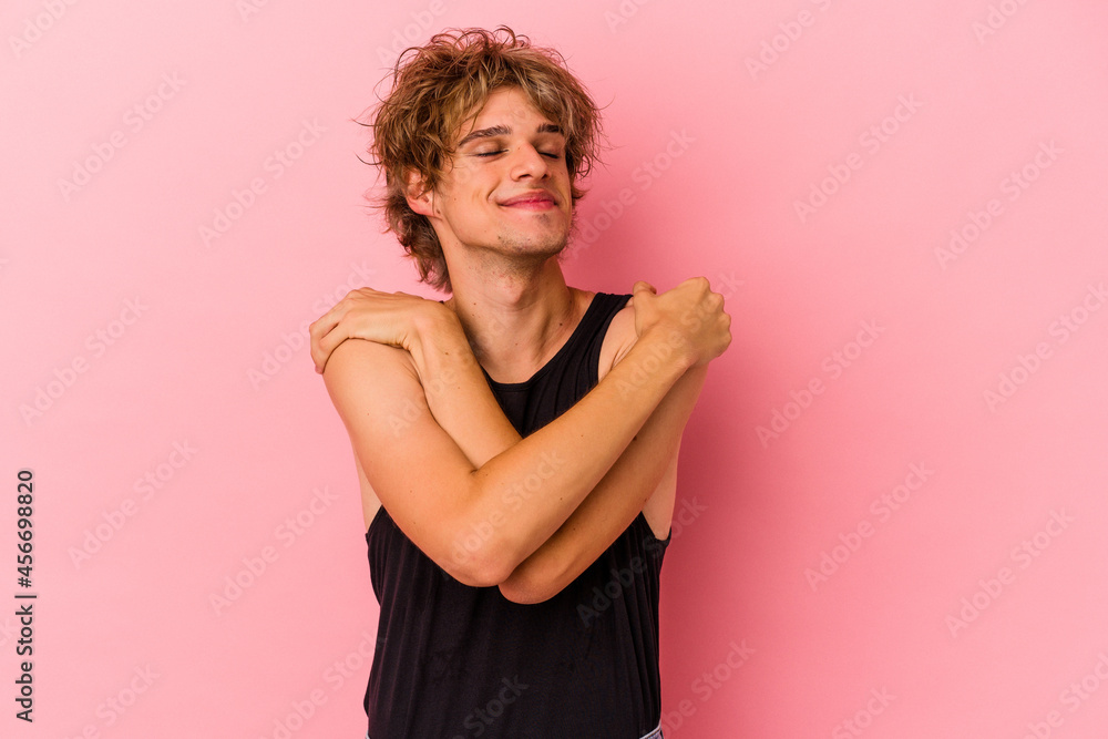 Young caucasian man with make up isolated on pink background hugs, smiling carefree and happy. Young caucasian man with make up isolated on pink background hugs, smiling carefree and happy.