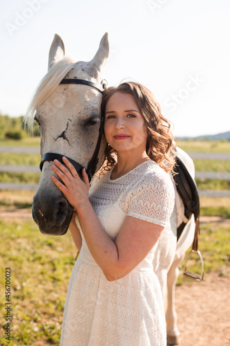Portrait of a young woman in a white dress hugging horse