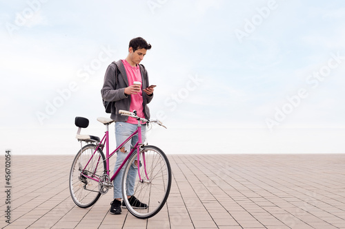 young man with bicycle and coffee looking phone