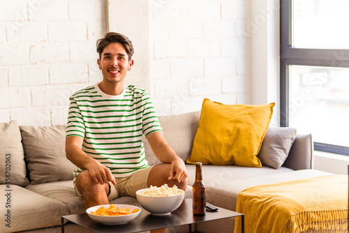 Young mixed race man eating popcorns sitting on the sofa happy, smiling and cheerful.
