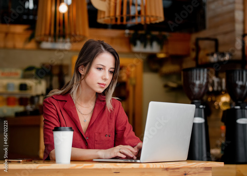 young woman using laptop computer drink a coffee sits at table in a cafe