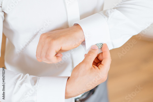 Preparing the grooms for the morning, a handsome man getting dressed and getting ready for the wedding, tightening cufflinks on a white shirt