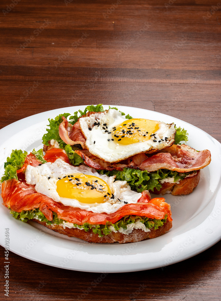 Toast with salmon, bacon and cream cheese. On a wooden background. Breakfast Toast with salmon, bacon and cream cheese. On a wooden background. Breakfast