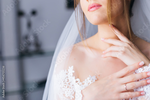 Morning of the bride. Portrait of a young beautiful tender bride with red lips in a white lace wedding dress gracefully put her hand on her neck.