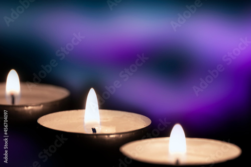 Three burning yellow candles on blurry purple background with copy space. Christmas candlelight in church for memorial day religious ritual, spiritual zen meditation, funeral worship ceremony.