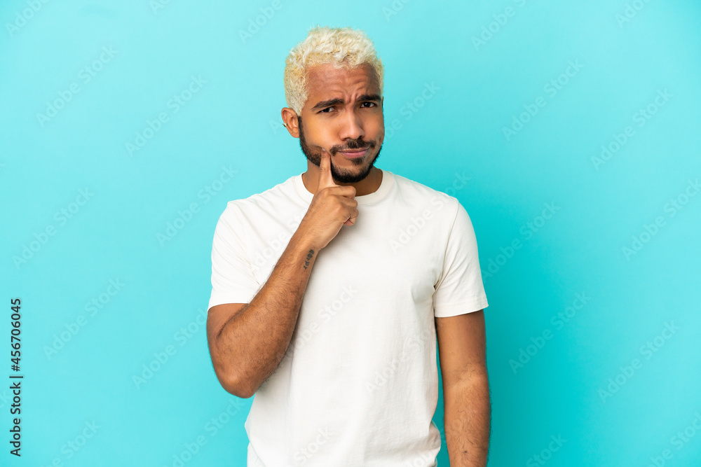 Young Colombian handsome man isolated on blue background and thinking