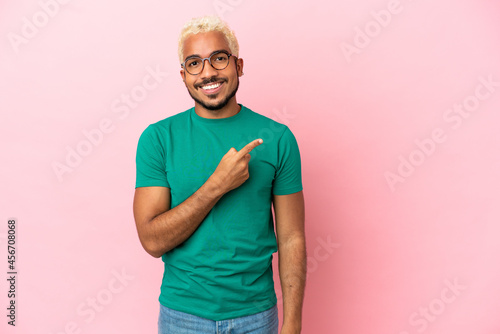 Young Colombian handsome man isolated on pink background pointing to the side to present a product