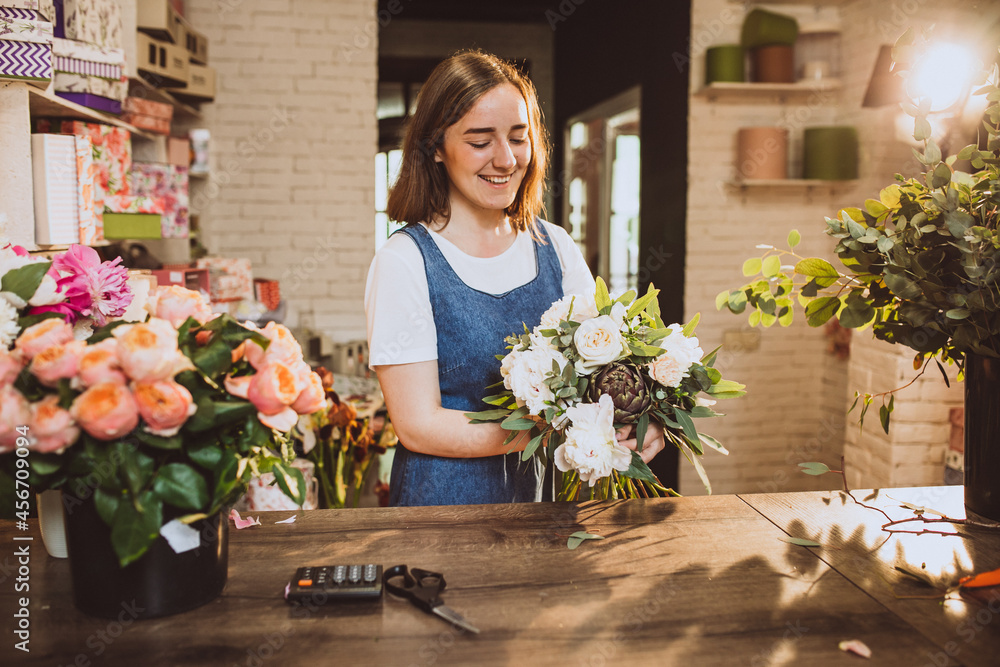 Woman florist at her own floral shop taking care of flowers - obrazy, fototapety, plakaty 