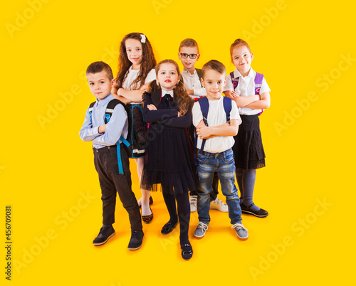 Obraz na plátne Schoochildren with backpacks and crossed hands standing over yellow background