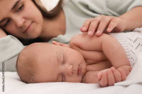 Young mother near her sleeping baby on bed, closeup