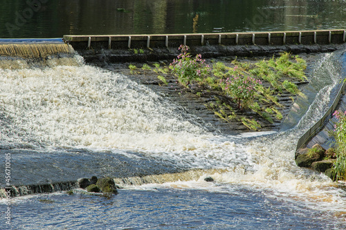 Cascade of white water flowing down a wide weir with a small narrow flow of water on the right along the River Wharfe, Otley, West Yorkshire, England, UK. photo