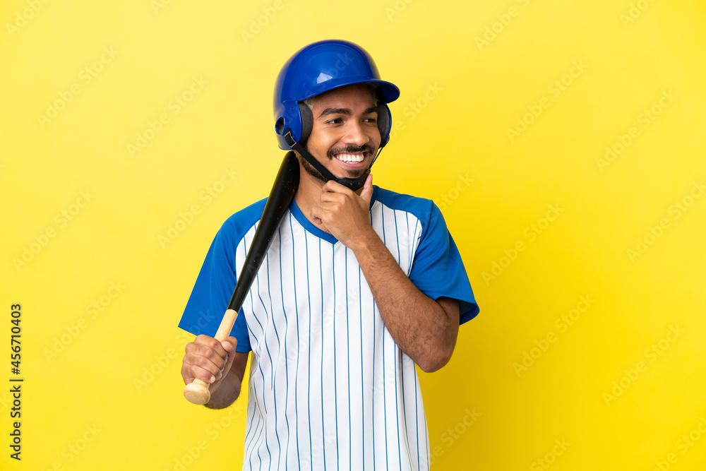 Young Colombian latin man playing baseball isolated on yellow background looking to the side and smiling