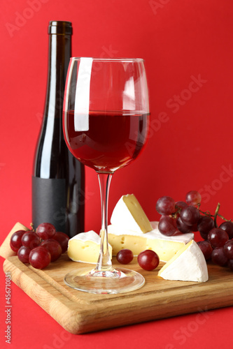 Board with wine  cheese and grape on red background