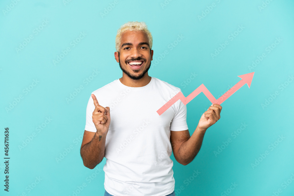 Fototapeta premium Young Colombian handsome man isolated on blue background holding a catching a rising arrow and pointing up