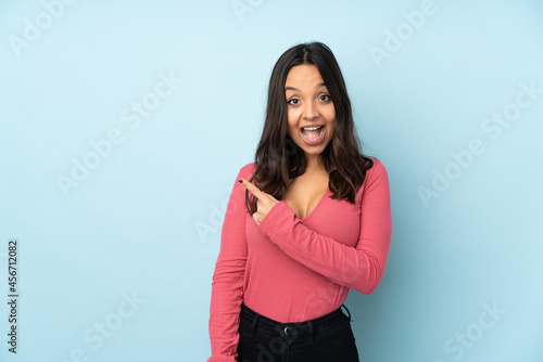 Young mixed race woman isolated on blue background surprised and pointing side