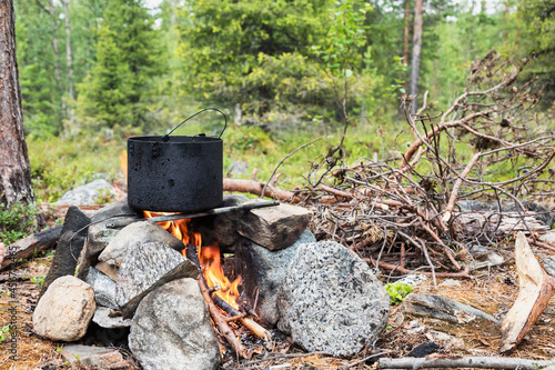 Cooking meal in a pot on burning campfire during wild camping in a forest