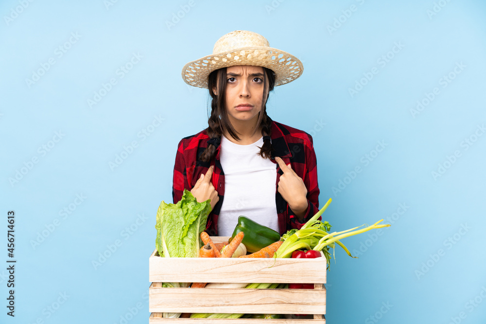 Young farmer Woman holding fresh vegetables in a wooden basket pointing to oneself