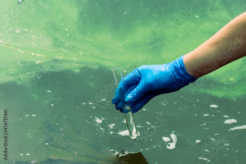 A gloved hand takes water into a test tube from a city reservoir. Urban waste water. Sampling from open water. Scientist or biologist takes a sample of water into a test tube