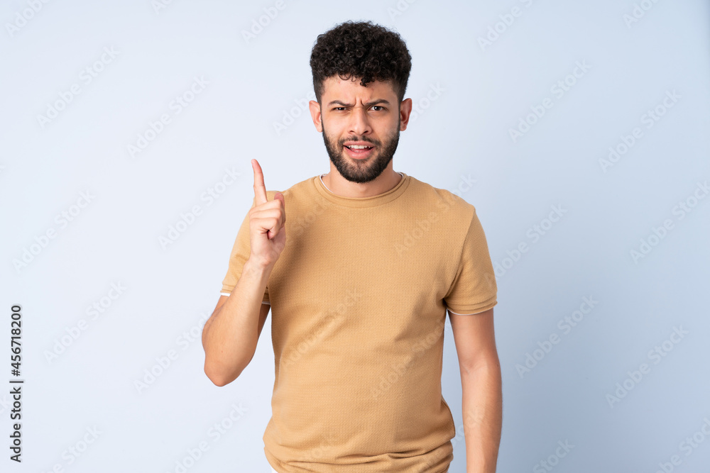 Young Moroccan man isolated on blue background intending to realizes the solution while lifting a finger up Young Moroccan man isolated on blue background intending to realizes the solution while lifting a finger up