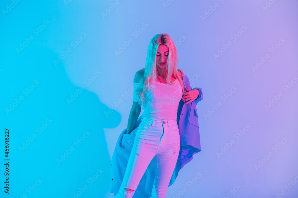 Fashionable young blonde woman in white stylish clothes wears blue blazer in studio with pastel neon and pink colors