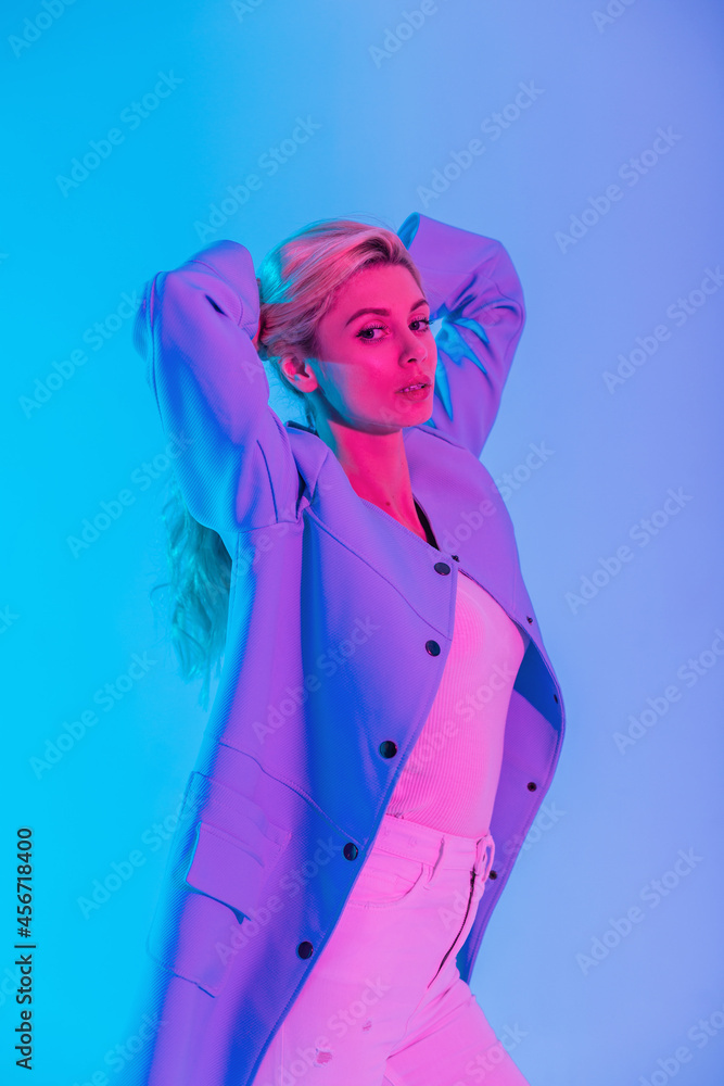 Fashion beauty girl model with stylish blue coat and white blouse with jeans indoors on colorful neon pink light Fashion beauty girl model with stylish blue coat and white blouse with jeans indoors on colorful neon pink light