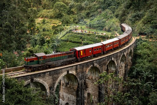 Red classic train on Nine arches bridge, running over ceylon tea plantation in Ella. Famous tourist attraction of Sri Lanka.