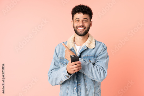 Young Moroccan man using mobile phone isolated on pink background pointing to the side to present a product © luismolinero
