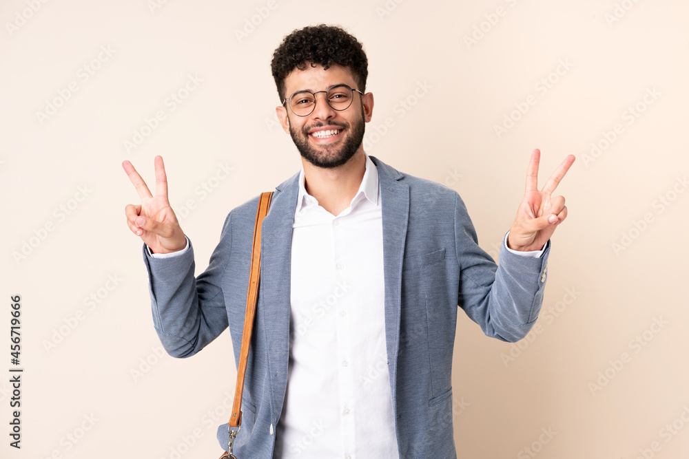 Young business Moroccan man isolated on beige background showing victory sign with both hands Young business Moroccan man isolated on beige background showing victory sign with both hands
