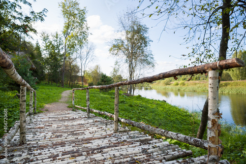 A wooden bridge made of birch logs on the bank of the river on a sunny day in the shade.