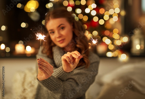 christmas, holidays and people concept - happy young woman with sparklers in bed at home bedroom at night over festive lights