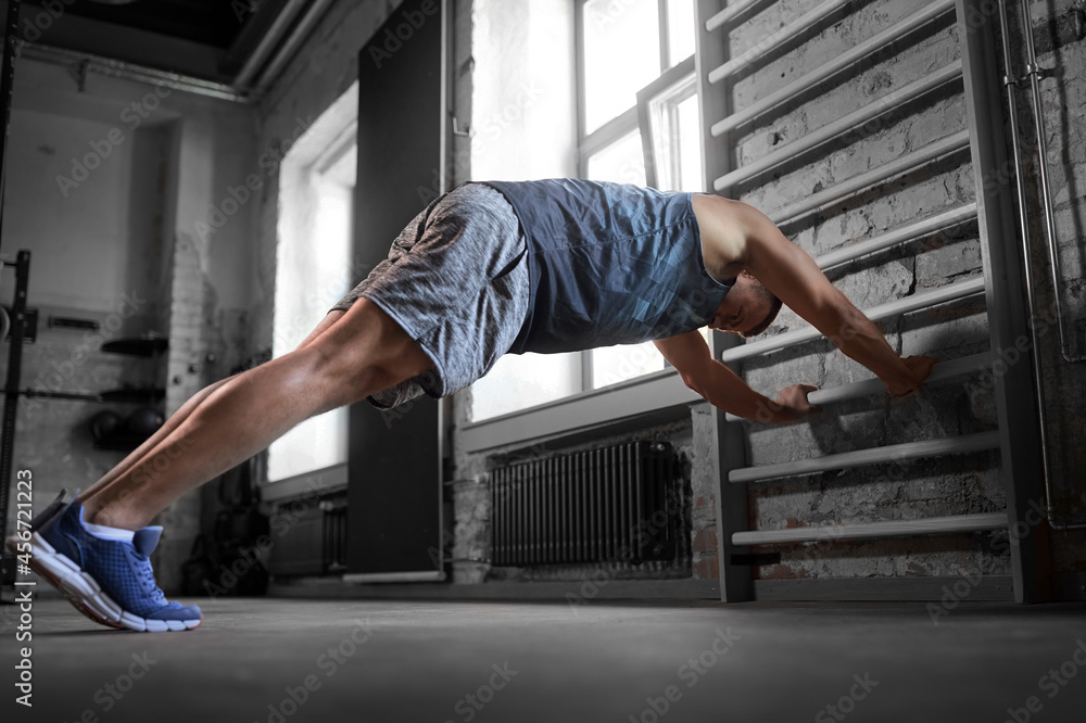 sport, bodybuilding, fitness and people concept - young man exercising on gymnastics wall bars in gym