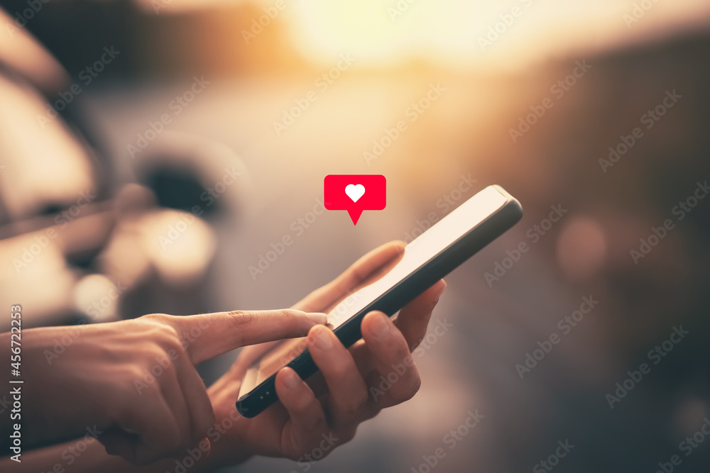 Close up woman hand hold using smart phone with heart icon at outdoor park street background. Copy space of technology business and travel holiday concept. - obrazy, fototapety, plakaty 