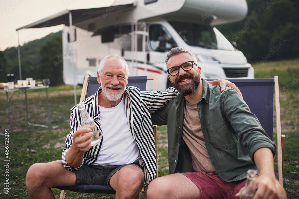 Mature man with senior father looking at camera at campsite outdoors, barbecue on caravan holiday trip. - obrazy, fototapety, plakaty 