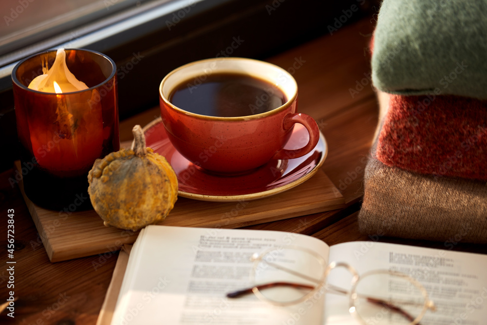 season and objects concept - open book with glasses, cup of coffee, autumn leaves, wool sweaters and candle burning on wooden window sill at home
