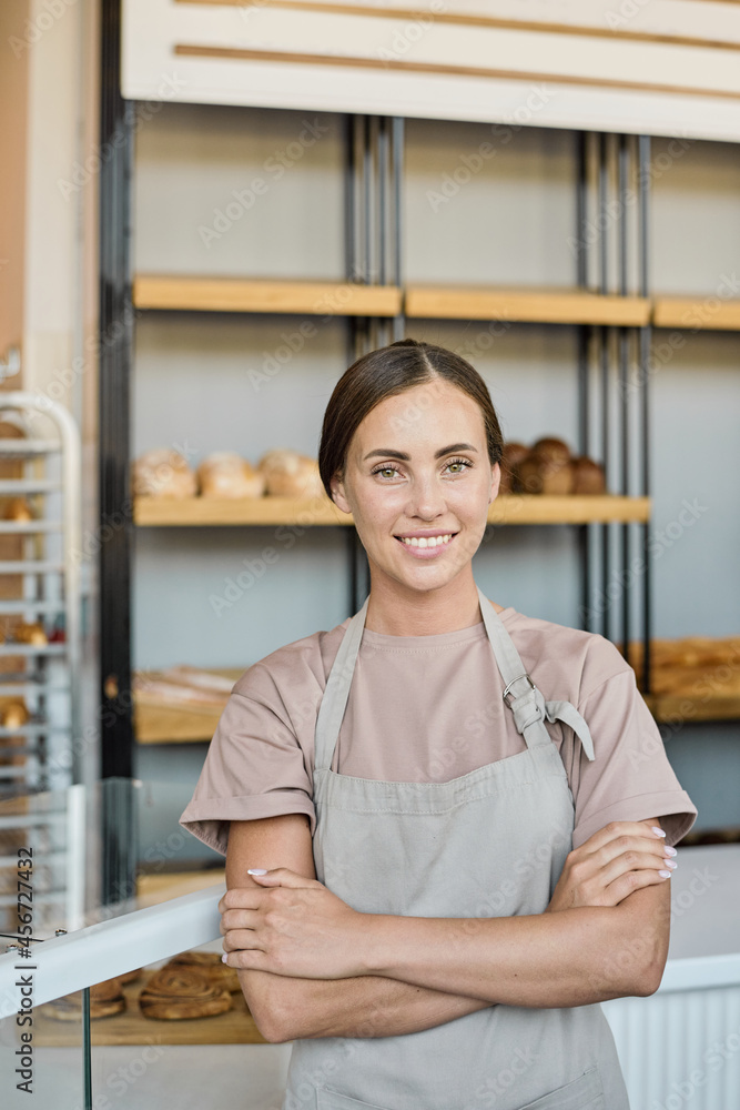 Portrait of happy young Caucasian owner of bakery standing with crossed arms against display with loaves of bread Portrait of happy young Caucasian owner of bakery standing with crossed arms against display with loaves of bread