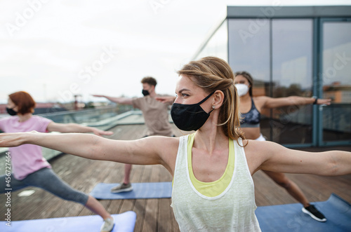 Group of young people with face masks doing exercise outdoors on terrace, coronavirus concept © Halfpoint