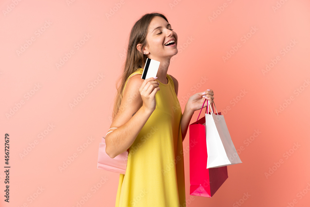 Young Lithuanian woman isolated on pink background holding shopping bags and a credit card Young Lithuanian woman isolated on pink background holding shopping bags and a credit card