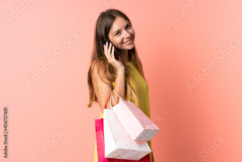 Young Lithuanian woman isolated on pink background holding shopping bags and calling a friend with her cell phone