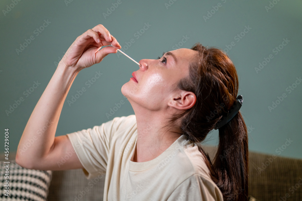 Obraz premium Asian woman using rapid antigen test kit for self test COVID-19 epidemic at home. Adult female unpacking a swab for inserts into her nose. COVID-19 coronavirus pandemic protection concept.