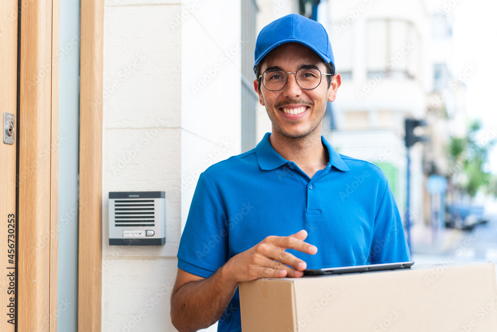 Young delivery man at outdoors holding boxes and a tablet with happy expression Young delivery man at outdoors holding boxes and a tablet with happy expression