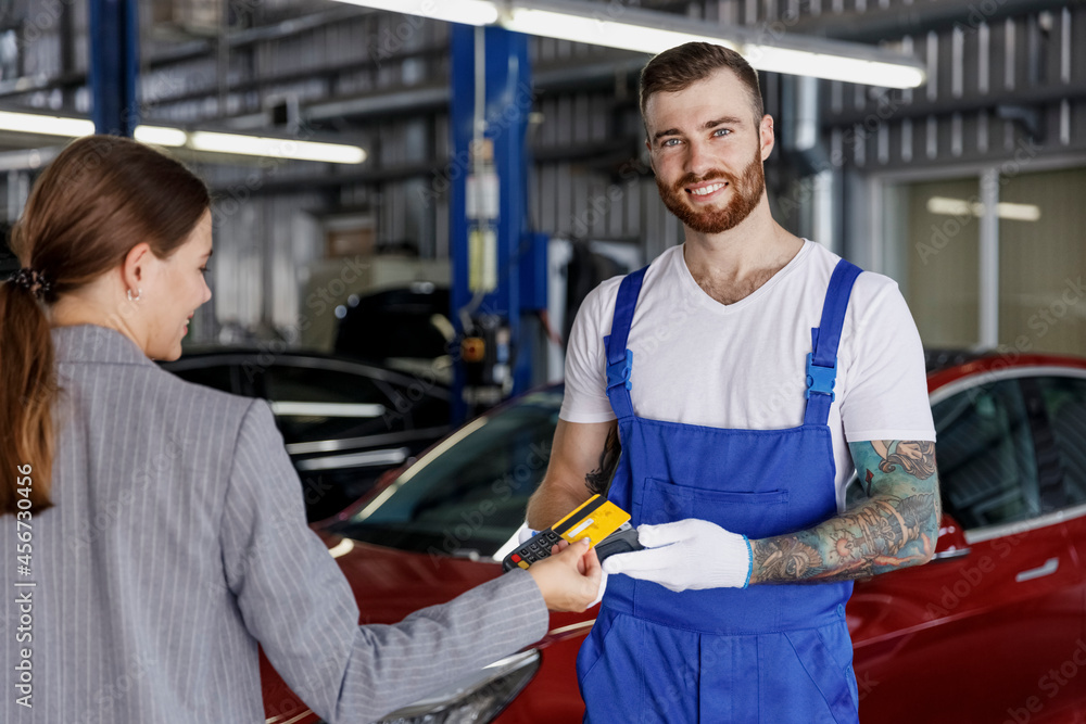 Foto Stock Young smiling happy professional car mechanic man in blue  overalls gloves hold payment terminal fow paying with credit card by female  owner driver woman work in vehicle repair shop workshop