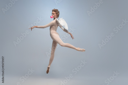 Full-length portrait of beautiful graceful ballerina dancing in image of angel with wings isolated on gray studio background. Art, motion, action, flexibility, inspiration concept.