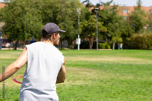 Young man with cap and no sleeves shirt playing with flying ring on sunny day at the park. Sports activity, recreation concepts
