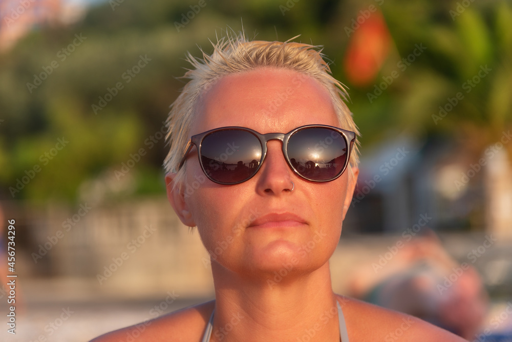 a woman with short blonde hair and sunglasses on beach