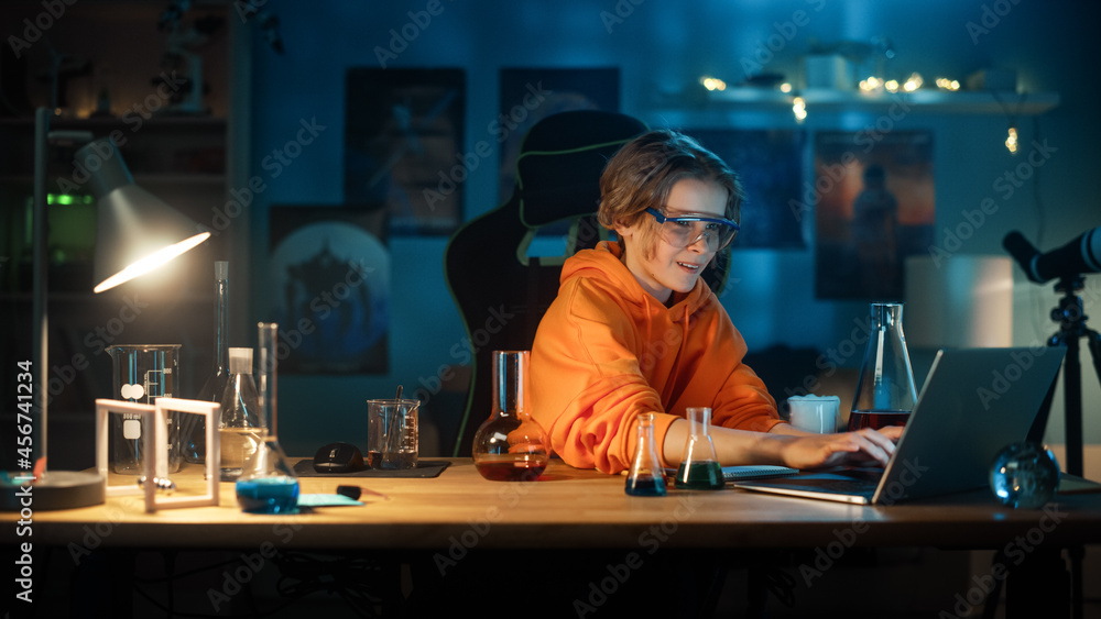 Smart Young Boy in Safety Goggles Write Down Results on a Laptop after Mixing Chemicals in Beakers. Teenager Conducting Educational Science Hobby Experiments, Doing Biology Homework in His Room.