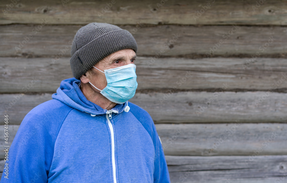 Older citizen in warm hat and medical face mask against wooden background. Older citizen in warm hat and medical face mask against wooden background.