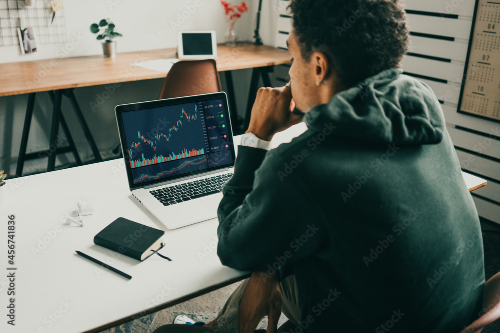 Investing in stock exchange market. Black man working remote using laptop. Back view Investing in stock exchange market. Black man working remote using laptop. Back view